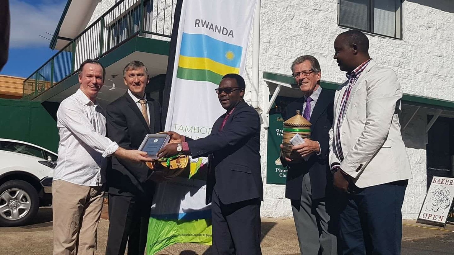 Philip shaking hands with the Rwandan ambassador and receiving an award outside the bakery during the Gold Coast Commonwealth Games