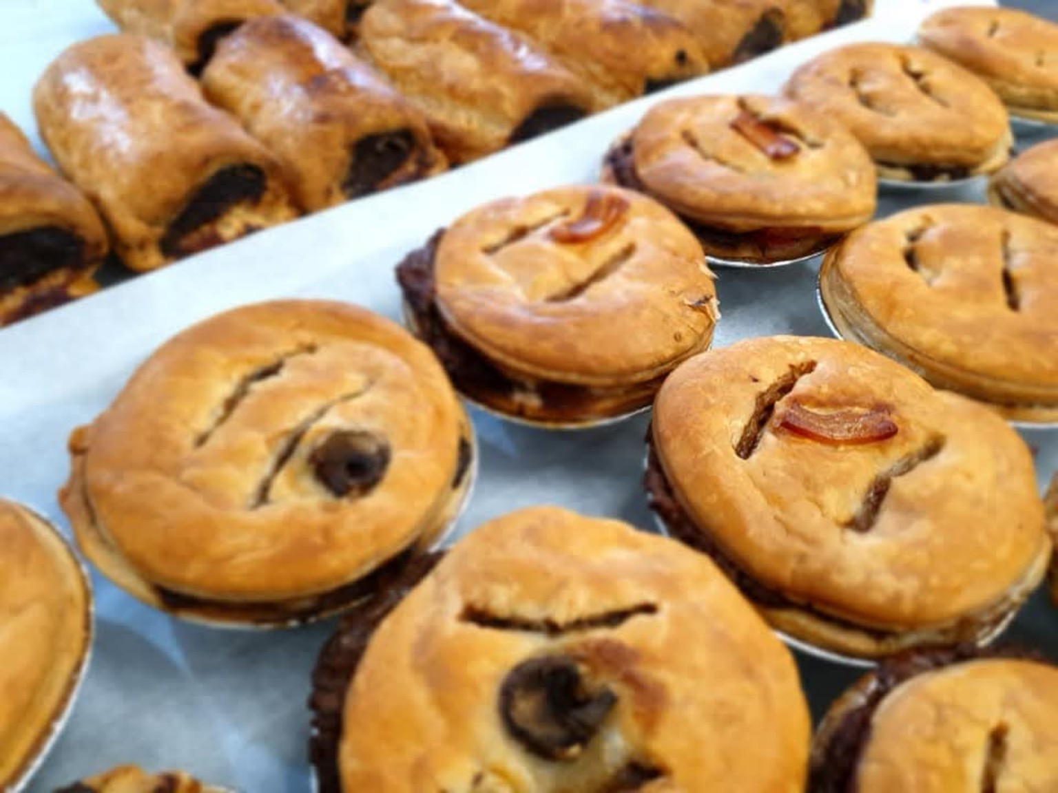 Golden baked pies with pastry rolls behind them
